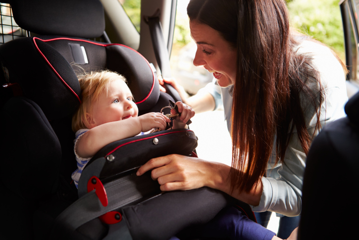 Mother Putting Daughter In Safety Seat On Car Journey